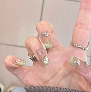 Detail von grünem Katzenaugen-Nageldesign mit silbernen 3D-Schmetterlingen und Perlen