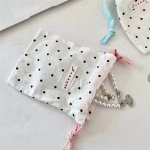 Detailed view of white polka dot drawstring pouch with a pearl necklace inside