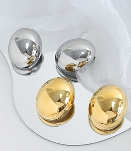 Detailed view of chunky oval earrings in polished gold and silver on a mirror tray
