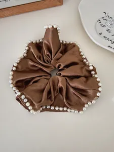 Detail of a brown satin scrunchie featuring elegant white pearl trim on a neutral background