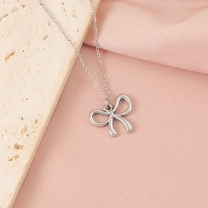 Vue détaillée du collier pendentif nœud argenté sur une pierre texturée et tissu rose doux