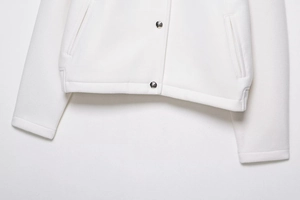 Close-up of white wool bomber jacket featuring gold buttons and refined pocket stitching