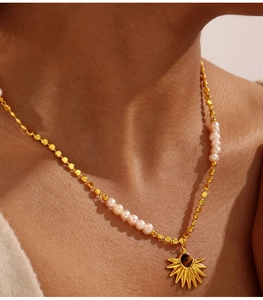 Close-up of gold chain necklace with freshwater pearls and tiger eye sunburst pendant