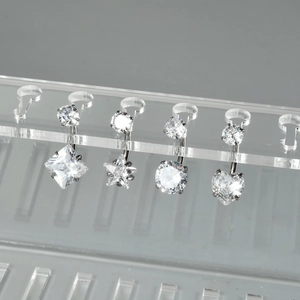 Detailed close-up of heart, star, square, and round zircon belly rings on acrylic stand