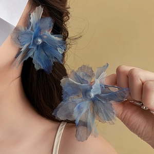 Detail of blue fabric flower earrings with pearls shown on model in warm soft lighting