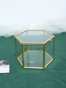 Macro detail of hexagonal glass jewelry box with gold metal frame and safety chain