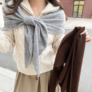 Détail d'un châle en tricot gris et d'une écharpe marron sur un pull en maille beige