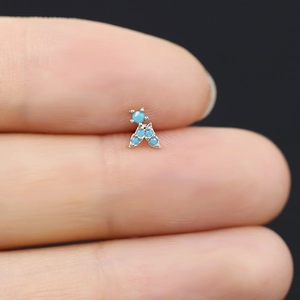 Vista macro di un minuscolo orecchino a perno in argento con pietre turchesi sulla punta del dito