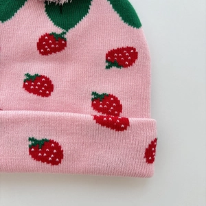 Close-up of pink strawberry knit hat with red jacquard patterns and soft fabric texture