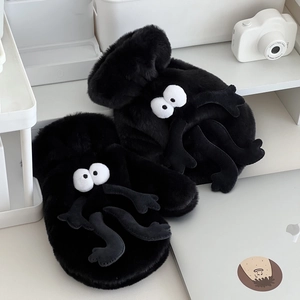 Close-up of black plush soot sprite mittens with cartoon eyes on a minimalist shelf