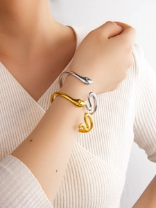 Polished snake shaped open bangle in gold and silver finish on female model wrist