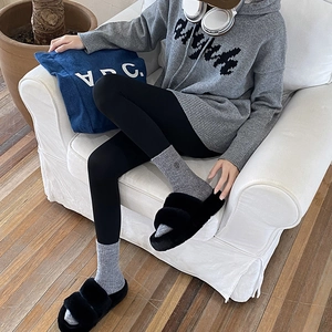 Close-up of black plush faux fur slippers worn by a model in a cozy indoor setting