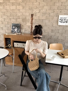 Close-up of a handmade woven straw bucket bag held by a model in a cafe setting