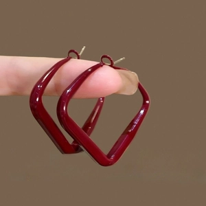 Boucles d'oreilles losanges géométriques rouge vin en résine tenues pour l'échelle