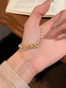 Detail of elegant gold bracelet with pearls and zircon charms on a wooden surface