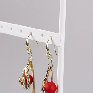 Detail of gold dangle earrings with red matte beads and tiny white zircons on a stand