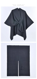 Detail view of black knit shawl with tassel trim and tie-front design on white background