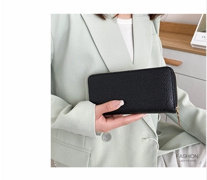 Close-up of black lychee grain long purse with gold zipper held by a fashion model