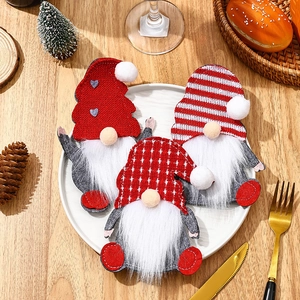 Three Christmas gnome cutlery holders with red knit hats on a white plate festive table decor
