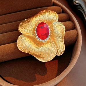 Macro view of vintage gold flower brooch with red gemstone in brown velvet box