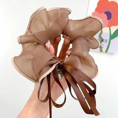 Close-up of brown sheer organza scrunchie featuring a ribbon bow and elegant pearl pendant