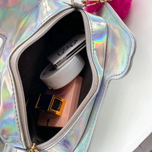 Detailed interior of holographic laser makeup bag showing cosmetics and pink pom pom