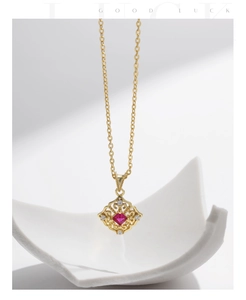 Close-up of gold pendant with red gemstone and white accents over ceramic