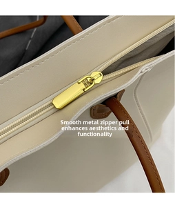 Detail of a gold polished metal zipper and fine stitching on a cream tote bag