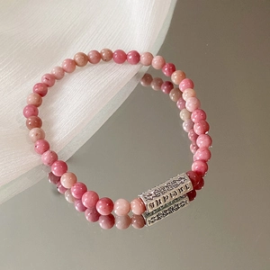 Makroaufnahme der rosa Perlenkette mit fein graviertem Silberanhänger auf Spiegelfläche