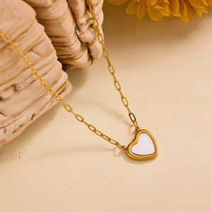 Dettaglio di una collana a catena a graffetta dorata con ciondolo a cuore in madreperla bianca