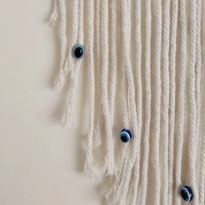 Close-up of handmade white cotton macrame wall hanging with blue evil eye bead detail