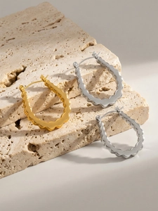 Macro detail of wavy U-shaped hoop earrings in gold and silver over travertine stone