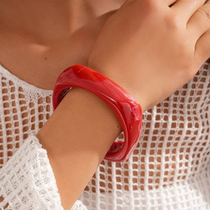 Detail of red irregular resin bangle worn with a white textured knit outfit