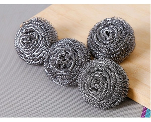 Detailed close-up of four stainless steel wire cleaning balls on a kitchen wooden board