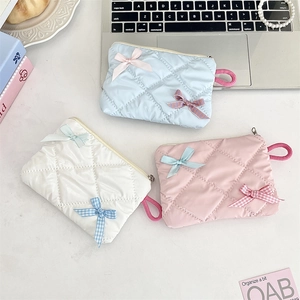 Three quilted cosmetic bags in blue, white, and pink with ribbon bow details and zip closure