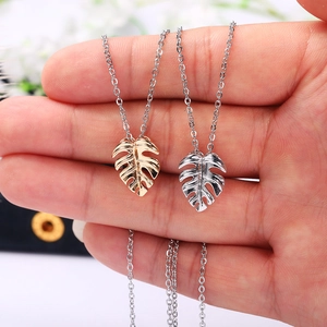 Detail of gold and silver monstera leaf pendants with fine engraving on delicate chains