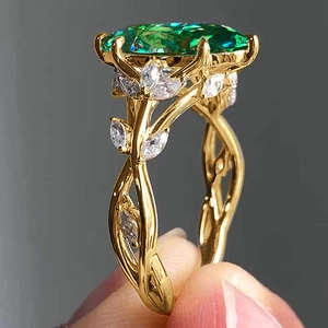 Macro detail of luxury gold leaf ring featuring a large emerald and diamond accents