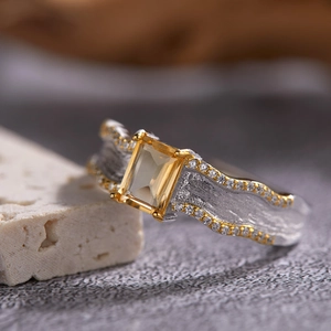 Macro shot of rectangular yellow gemstone ring with textured gold and silver metal bands