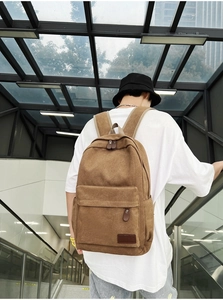 Rear view of a model wearing a brown canvas backpack featuring a front zipper pocket