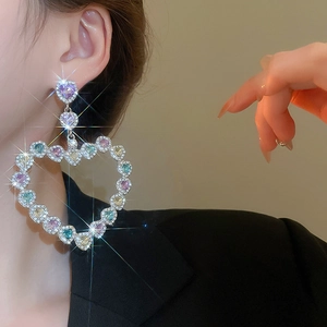 Détail de boucles d'oreilles cœur évidées avec pierres multicolores et cristaux étincelants