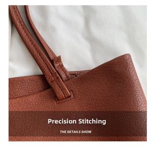 Detail of reinforced stitching and litchi grain leather texture on brown tote bag