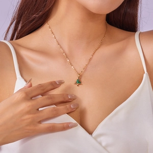 Detail of a gold Christmas tree pendant necklace with red and green gemstones on a model