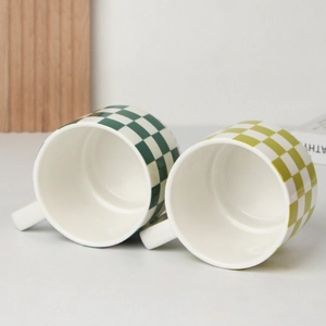 Detailed view of ceramic mugs featuring green and yellow checkered patterns on a white table