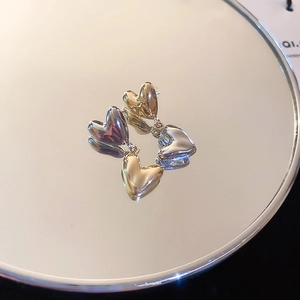 Macro shot of 3D metallic heart earrings with gold and silver finish on a mirror