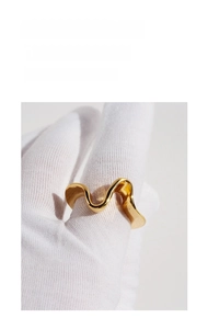 Close-up of a wavy gold plated brass ring with a polished finish on a gloved hand