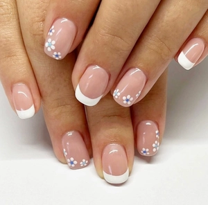 Close-up of white French tip press-on nails with blue-centered daisy patterns