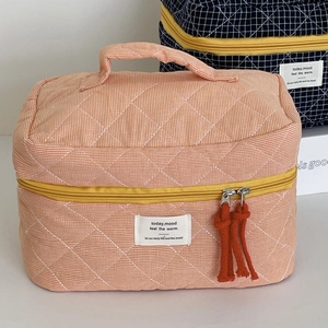 Close-up of quilted orange grid toiletry bag with cotton tassel and stitched brand label