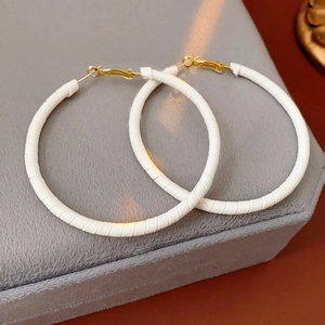 Detail of white textured hoop earrings with gold clasp on grey velvet display stand