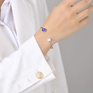 Close-up of a silver-tone evil eye cuff bracelet with a blue eye and pearl on a model