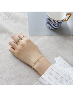 Elegant gold pearl bracelet and rings worn by a model on light linen background